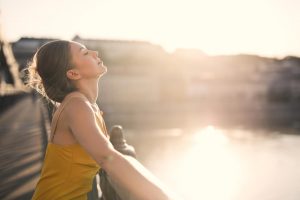 Jovem mulher apoiada no corrimão de uma ponte enquanto aproveita o sol para estimular o autocuidado.