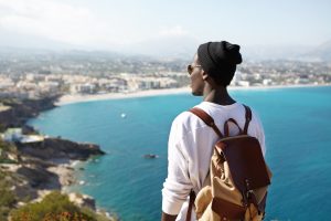 Jovem negro de costas, admirando a vista do litoral e aproveitando a liberdade de viajar sozinho.