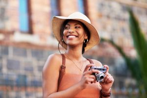 Jovem mulher negra com uma câmera em mãos, feliz em viajar por São Paulo.